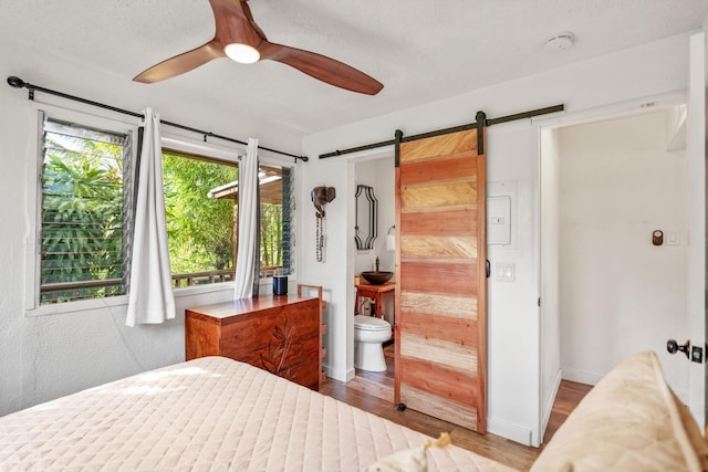 bedroom featuring a barn door, ceiling fan, ensuite bath, and hardwood / wood-style flooring