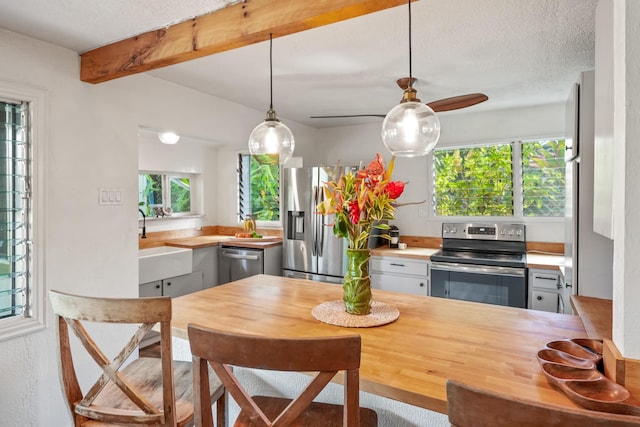 kitchen with sink, stainless steel appliances, beamed ceiling, pendant lighting, and a textured ceiling