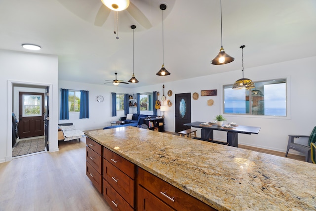 kitchen featuring light stone countertops, light wood-type flooring, hanging light fixtures, and ceiling fan