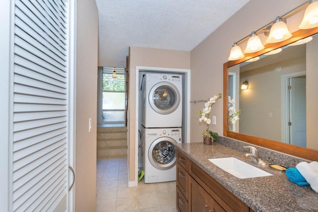 clothes washing area with a textured ceiling, sink, light tile patterned floors, and stacked washer / drying machine