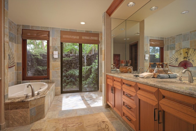 bathroom featuring a relaxing tiled tub, vanity, and tile walls