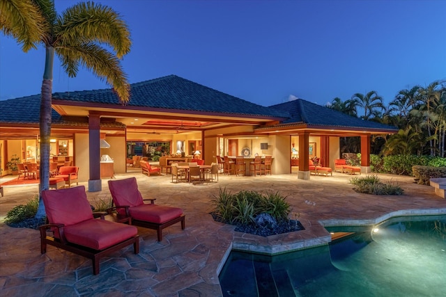 pool at dusk with exterior bar and a patio area