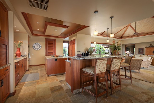 interior space with a breakfast bar area, hanging light fixtures, a tray ceiling, a kitchen island, and kitchen peninsula