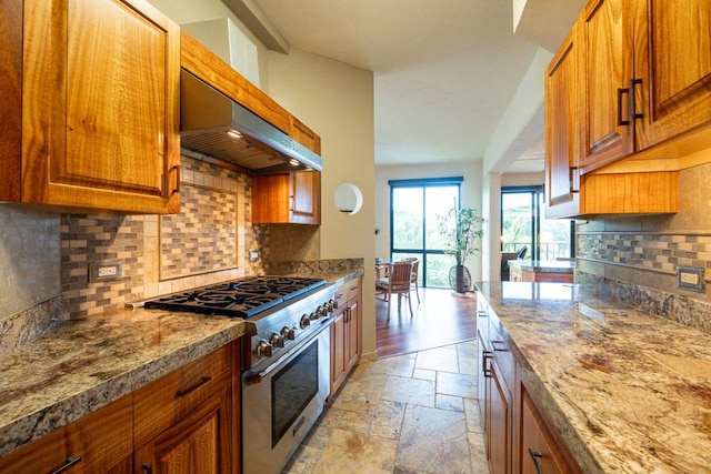 kitchen featuring light stone countertops, decorative backsplash, stainless steel stove, and ventilation hood