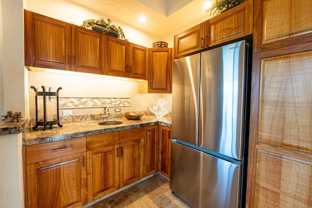 kitchen with dark stone counters, stainless steel fridge, tasteful backsplash, and sink