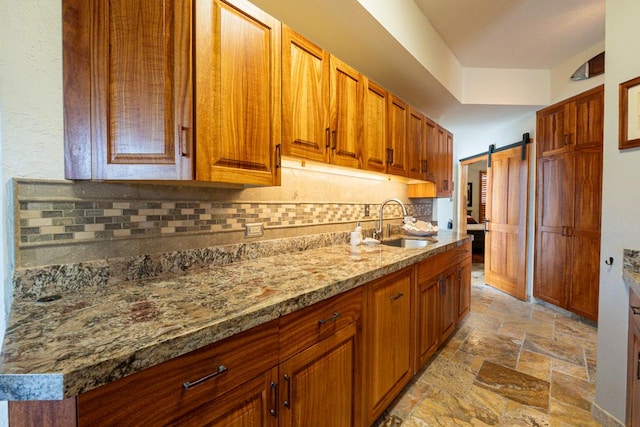 kitchen with sink, stone countertops, tasteful backsplash, and a barn door