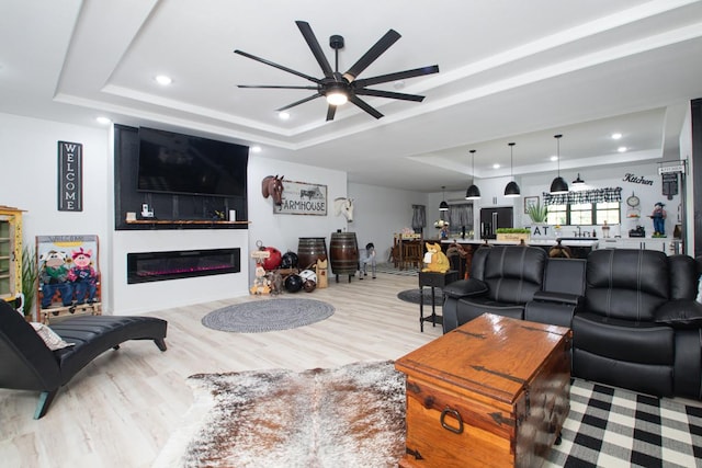 living room featuring ceiling fan, a raised ceiling, and light hardwood / wood-style flooring