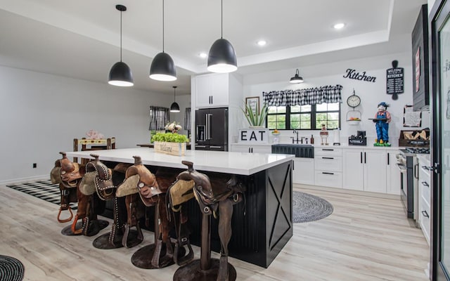 kitchen featuring a center island, premium appliances, white cabinets, decorative light fixtures, and a raised ceiling