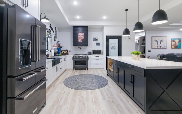 kitchen with pendant lighting, high quality appliances, sink, white cabinets, and light hardwood / wood-style floors