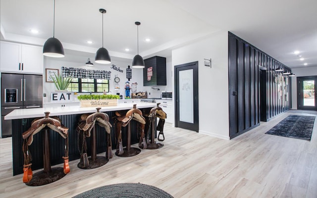 kitchen with a spacious island, hanging light fixtures, white cabinets, light wood-type flooring, and high quality fridge