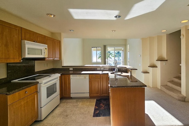 kitchen featuring sink, dark stone countertops, a center island, light tile patterned floors, and white appliances