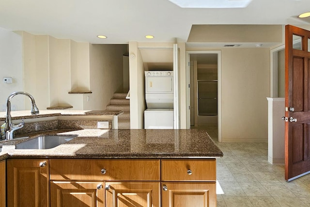 kitchen featuring light tile patterned flooring, stacked washer / drying machine, sink, and dark stone counters