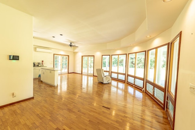 unfurnished living room with ceiling fan, light wood-style flooring, baseboards, french doors, and a wall mounted air conditioner