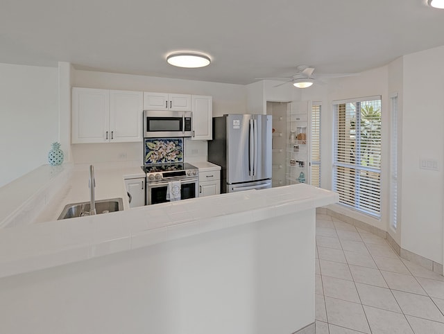 kitchen with white cabinetry, tile countertops, kitchen peninsula, appliances with stainless steel finishes, and sink