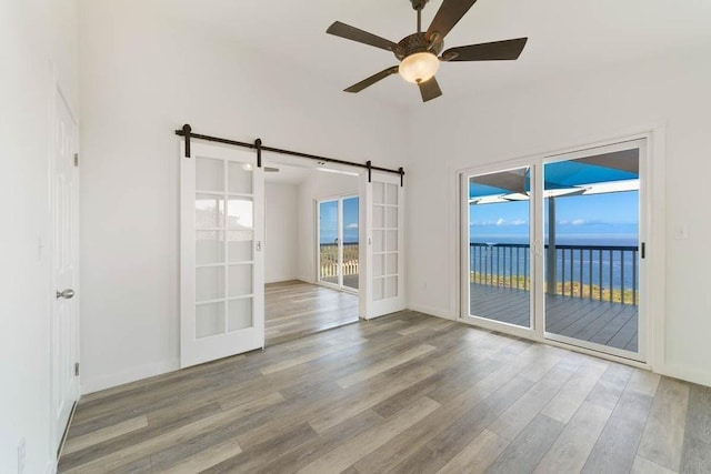 unfurnished room featuring a barn door, ceiling fan, a water view, and a healthy amount of sunlight