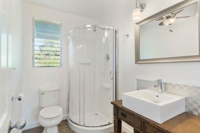 bathroom featuring ceiling fan, tasteful backsplash, toilet, vanity, and a shower with shower door