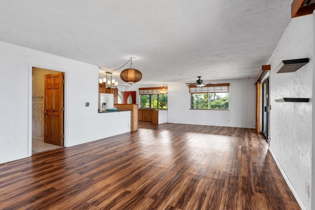 unfurnished living room featuring a textured ceiling, ceiling fan with notable chandelier, and dark hardwood / wood-style floors