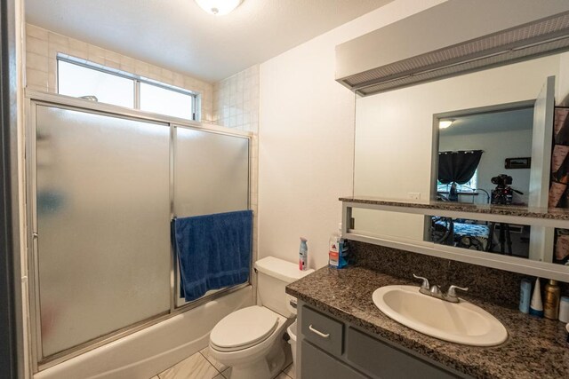 full bathroom with tile patterned floors, shower / bath combination with glass door, vanity, and toilet