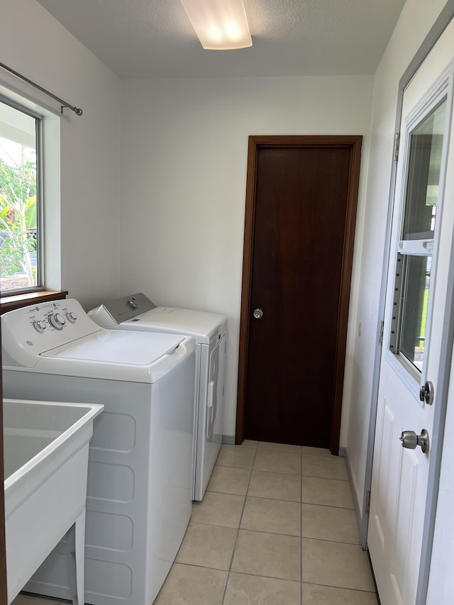 clothes washing area featuring sink, light tile patterned flooring, separate washer and dryer, and a textured ceiling