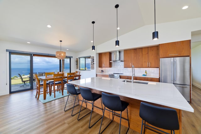 kitchen featuring sink, wall chimney range hood, appliances with stainless steel finishes, a water view, and decorative light fixtures