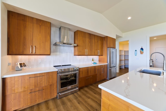 kitchen featuring vaulted ceiling, tasteful backsplash, sink, stainless steel appliances, and wall chimney range hood