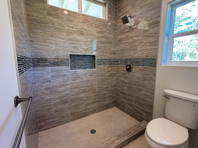 bathroom with a tile shower, toilet, and a healthy amount of sunlight