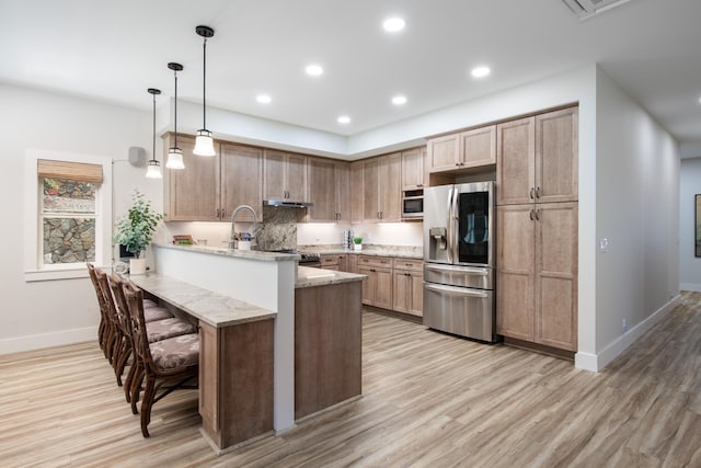 kitchen with a kitchen breakfast bar, stainless steel fridge with ice dispenser, light stone counters, kitchen peninsula, and pendant lighting