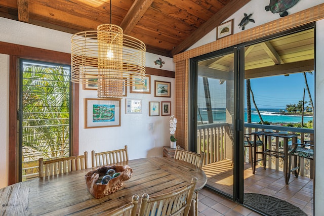 dining area with a water view, an inviting chandelier, lofted ceiling with beams, light tile patterned floors, and wooden ceiling