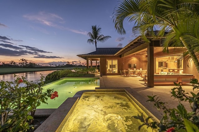 pool at dusk with a jacuzzi, a water view, outdoor lounge area, and a patio area