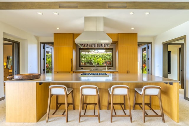 kitchen with a spacious island, a kitchen breakfast bar, stainless steel gas cooktop, and island range hood