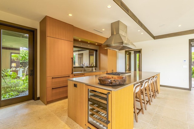 kitchen with a spacious island, sink, island exhaust hood, a kitchen bar, and beverage cooler