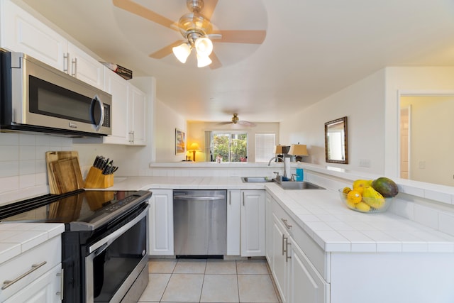 kitchen with appliances with stainless steel finishes, tile counters, white cabinets, and kitchen peninsula