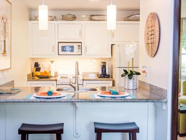 kitchen featuring white cabinetry, a breakfast bar, pendant lighting, and white appliances