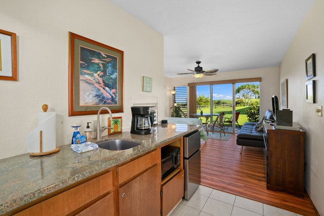 kitchen featuring refrigerator, sink, ceiling fan, light stone countertops, and light tile patterned floors