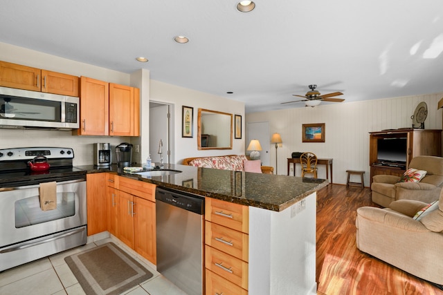 kitchen with sink, kitchen peninsula, dark stone countertops, light tile patterned flooring, and appliances with stainless steel finishes