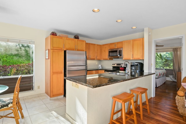 kitchen with sink, dark stone countertops, light tile patterned flooring, kitchen peninsula, and stainless steel appliances