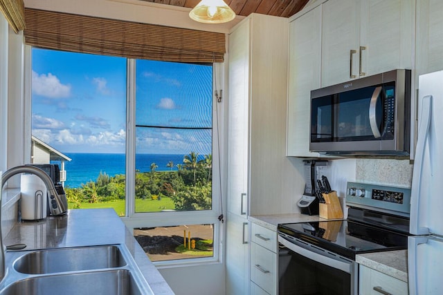 kitchen featuring sink, backsplash, light stone counters, stainless steel appliances, and a water view