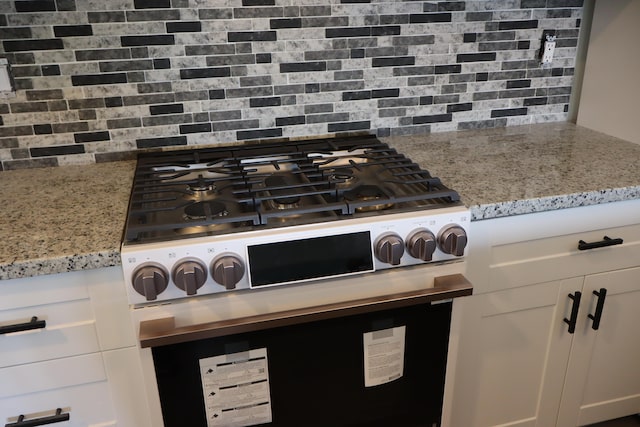 interior details with white cabinets, tasteful backsplash, light stone countertops, and stainless steel gas range