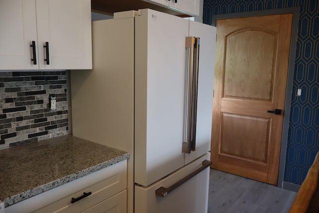 kitchen with light stone countertops, light wood-type flooring, refrigerator, tasteful backsplash, and white cabinets