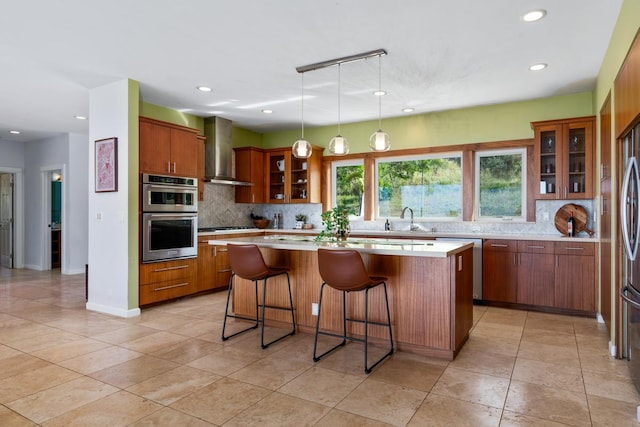 kitchen featuring decorative light fixtures, backsplash, wall chimney range hood, and a kitchen island