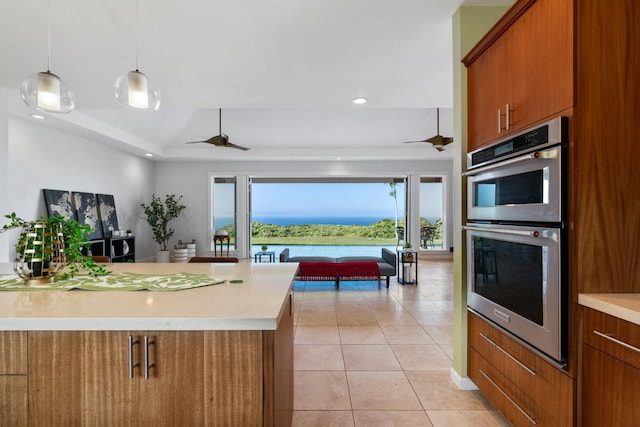 kitchen with light tile patterned floors, ceiling fan, double oven, pendant lighting, and a water view