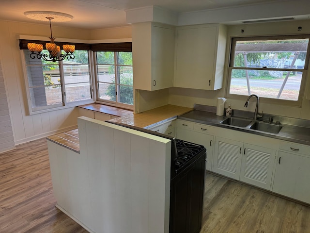 kitchen with sink, a chandelier, light wood-type flooring, kitchen peninsula, and pendant lighting