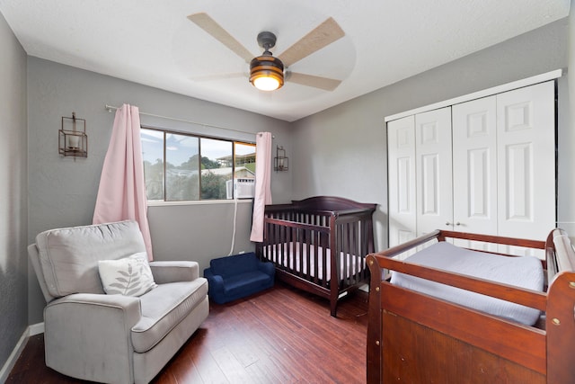 bedroom featuring ceiling fan, a crib, dark wood-type flooring, and a closet