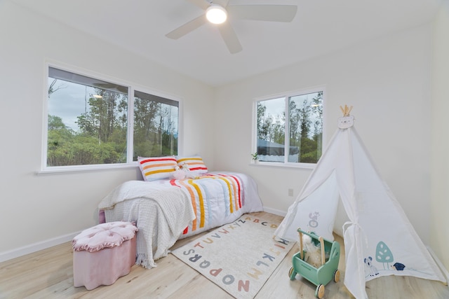 bedroom with ceiling fan, multiple windows, and light hardwood / wood-style flooring