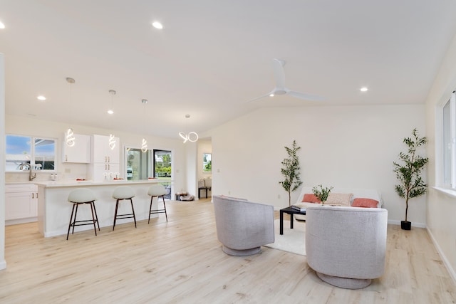 living room with light wood-type flooring, vaulted ceiling, ceiling fan, and sink