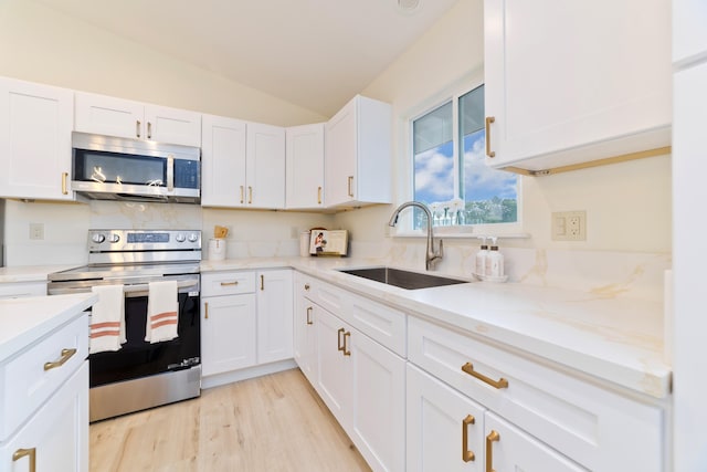 kitchen featuring appliances with stainless steel finishes, vaulted ceiling, sink, light hardwood / wood-style flooring, and white cabinets