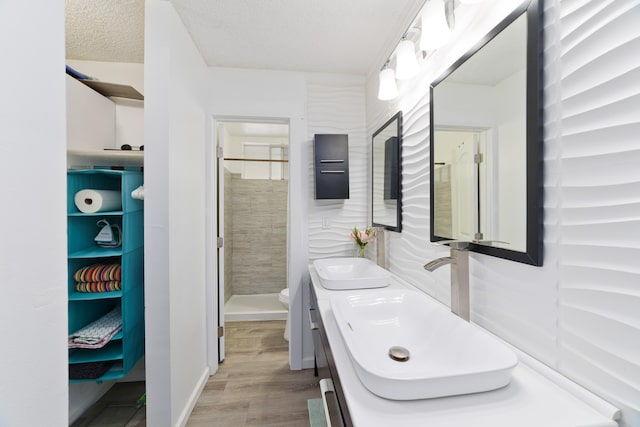 bathroom featuring toilet, wood-type flooring, a textured ceiling, a tile shower, and vanity