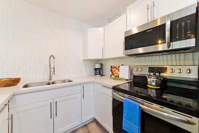 kitchen featuring sink, white cabinetry, backsplash, stainless steel appliances, and light wood-type flooring