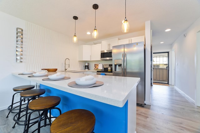 kitchen with sink, a breakfast bar area, white cabinetry, stainless steel appliances, and decorative light fixtures