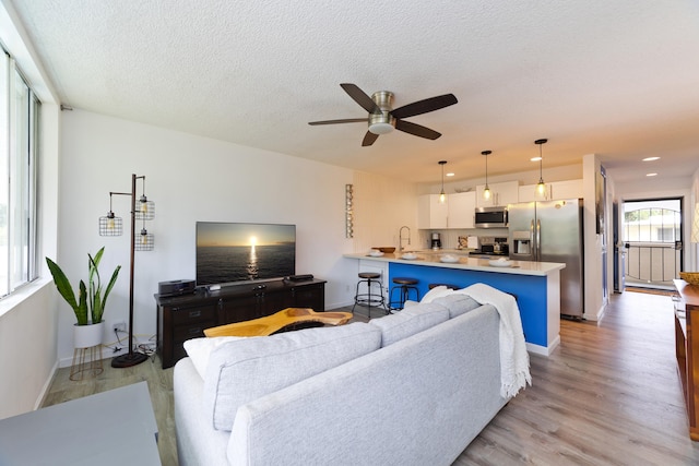 living room featuring sink, a textured ceiling, light hardwood / wood-style floors, and ceiling fan